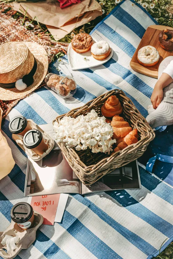 A picnic blanket with croissants, coffee and a straw hat